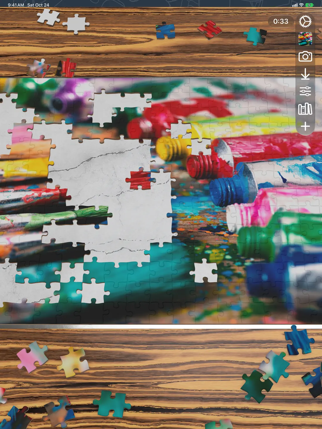 A puzzle of paint tubes partly assembled on iPad, on a striped wood board