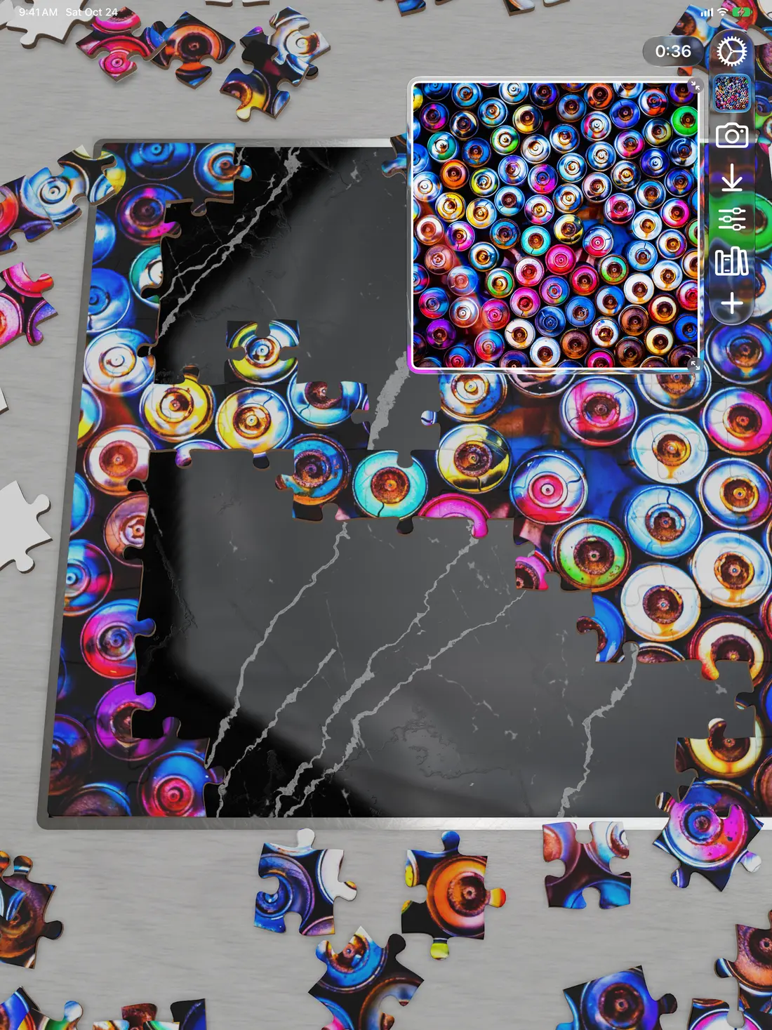 A puzzle of colorful spray-can tops partly assembled on iPad, on a gray board